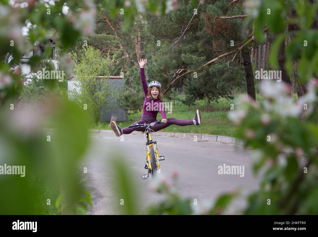 drôle de jeune femme émotive dans un casque sur un vélo.Équilibre, jambes écartées, cyclisme. Mode de vie actif sain, bien-être, sport Banque D'Images