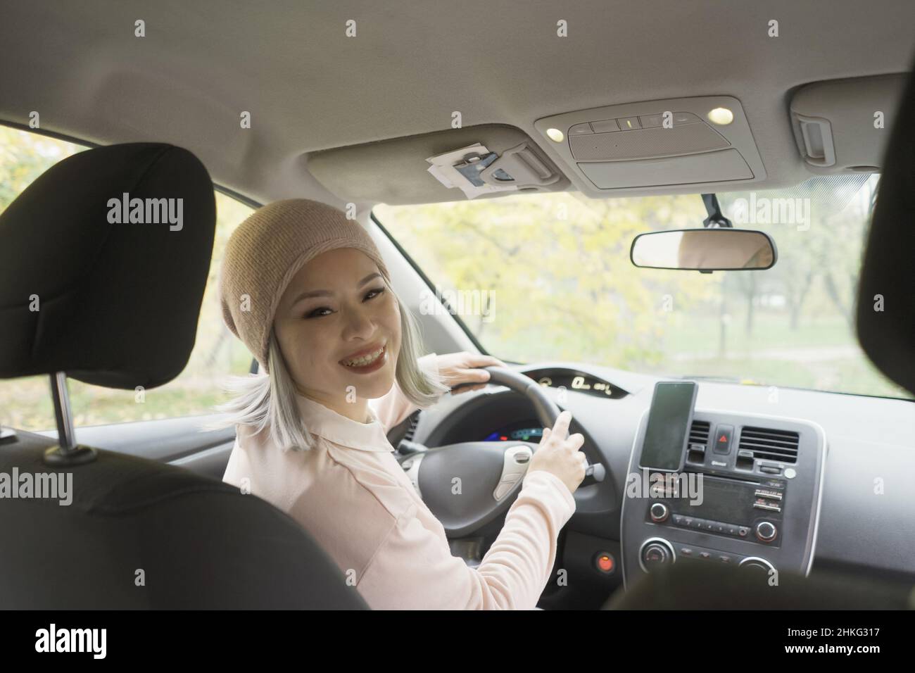 Portrait asiatique femme regardant de haut en arrière de la voiture.Femme asiatique mûre regardant l'enfant ou le passager tenant un volant.Femme asiatique blonde d'âge moyen dans la voiture. Banque D'Images