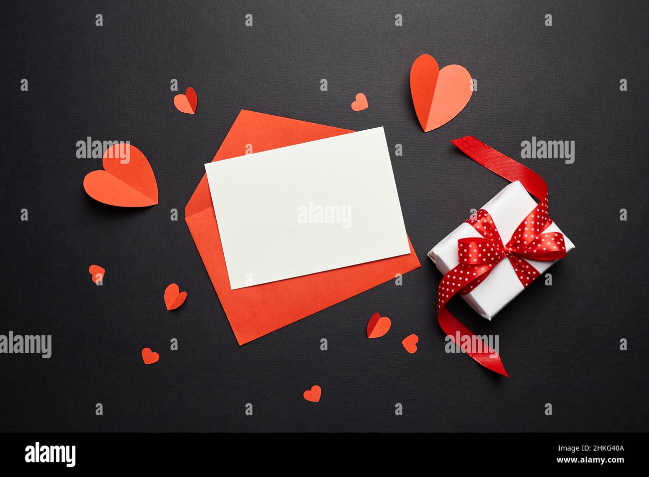Maquette de carte de vœux et boîte cadeau avec décorations en papier sur fond noir. Carte de vœux ou invitation vierge, enveloppe et coeurs en papier rouge Banque D'Images