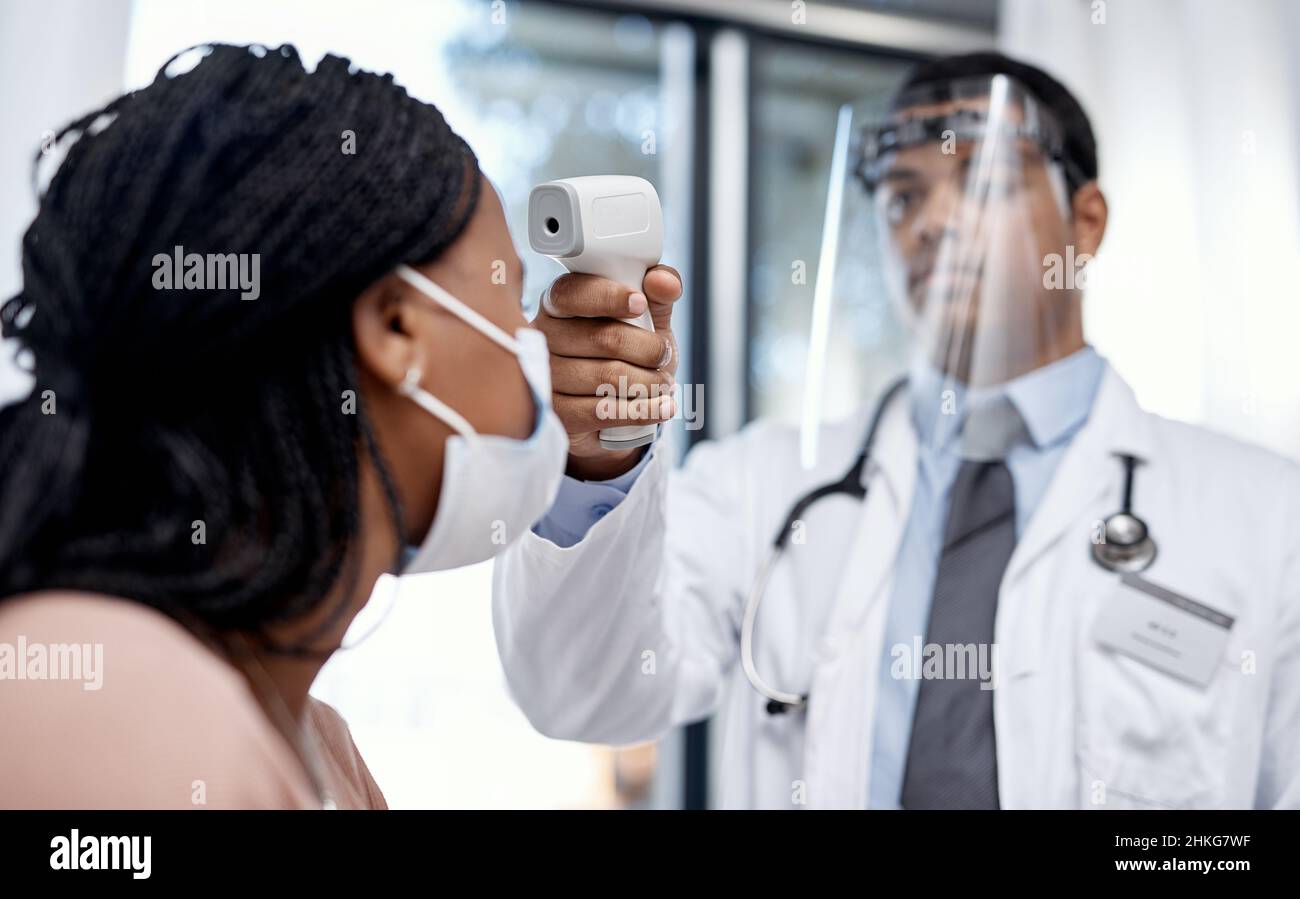 Être protégé pour la sécurité de tous.Prise de vue d'un médecin prenant la température d'un patient avec un thermomètre infrarouge. Banque D'Images