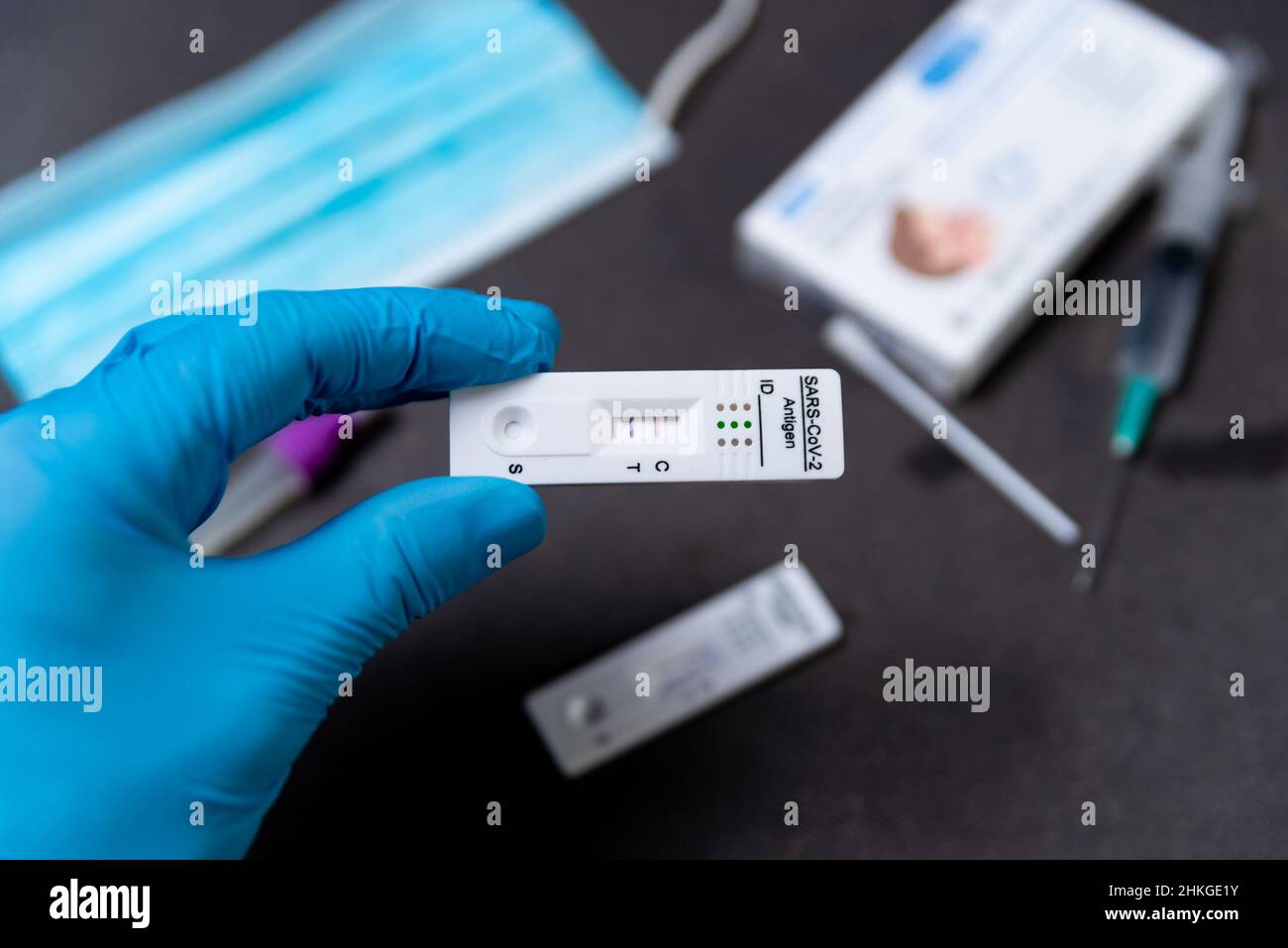 Une main portant un gant de protection est considérée en tenant un test Covid rapide, également appelé test d'antigène ou test de flux latéral, montrant un résultat positif dans un Banque D'Images