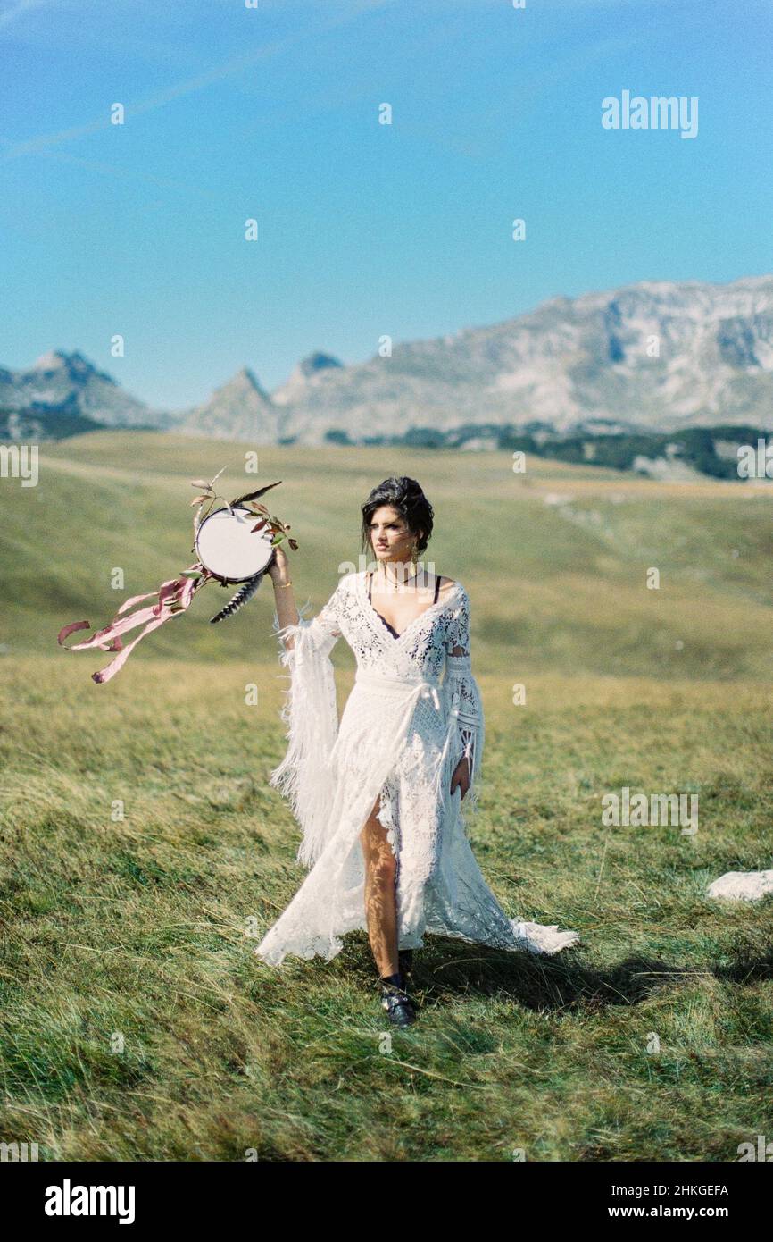 Fille avec un tambourin dans sa main marche à travers une vallée verte avec la toile de fond des montagnes Banque D'Images