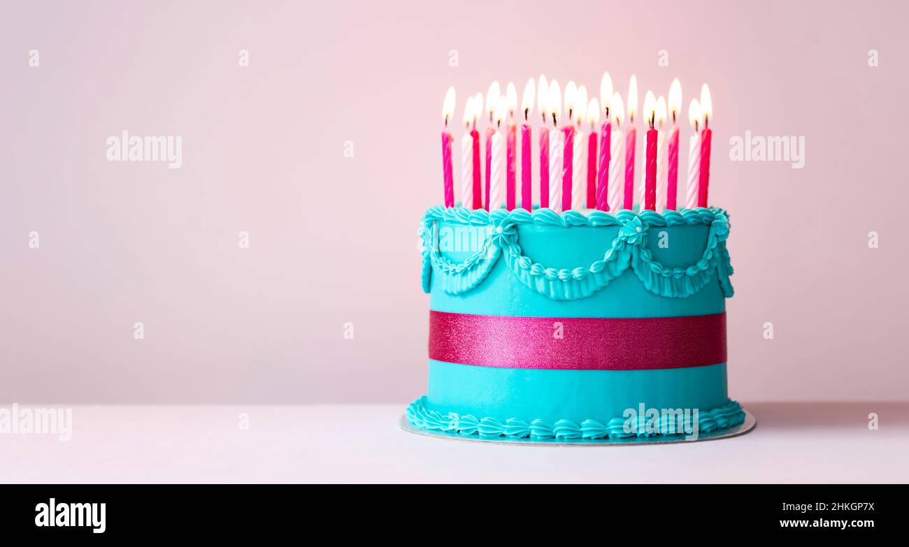 Gâteau d'anniversaire bleu avec passepoil de crème au beurre, ruban rose et bougies d'anniversaire roses Banque D'Images