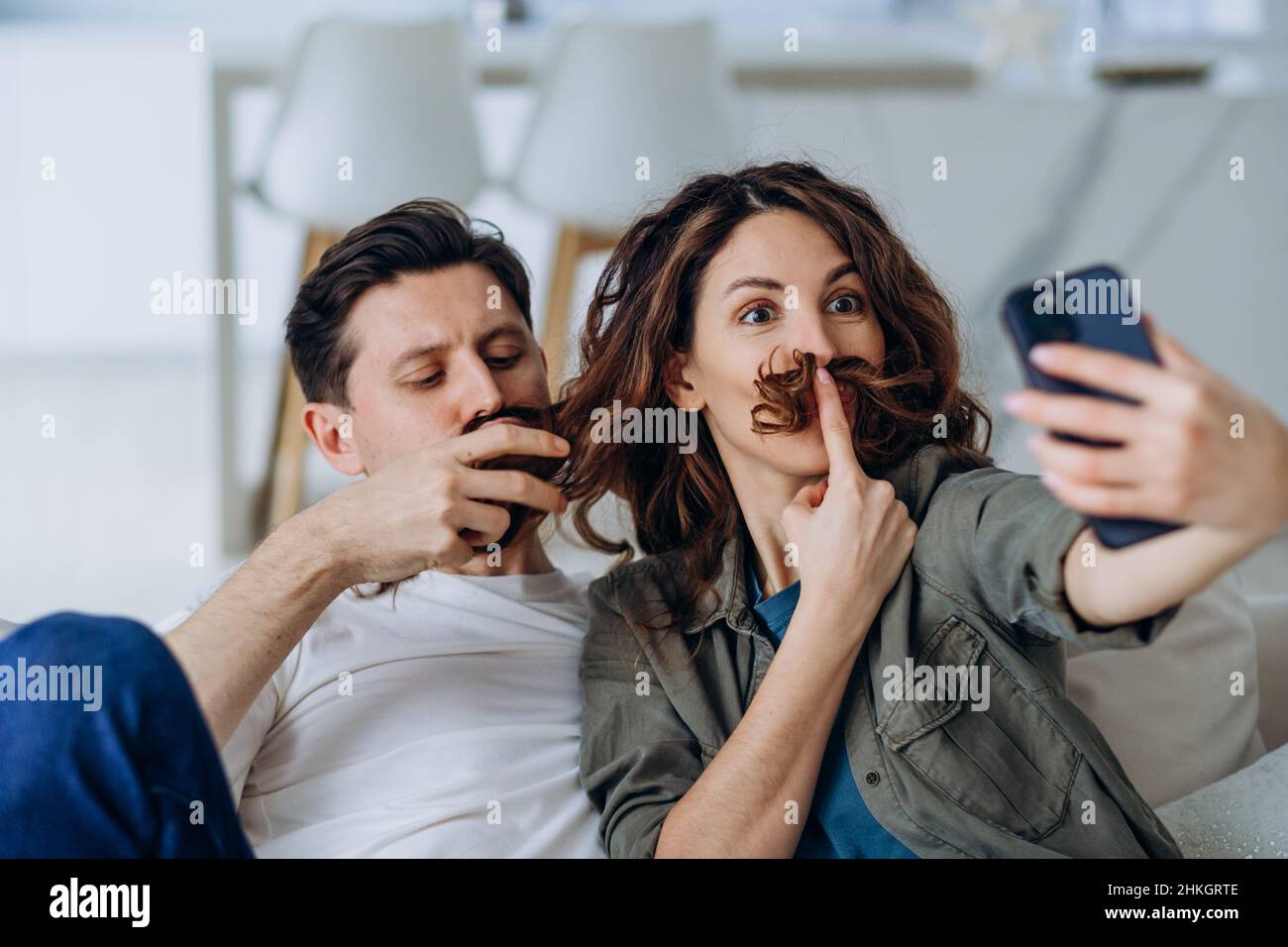 Une brune souriante et un jeune homme aux cheveux courts se posent avec des cheveux bouclés comme une moustache pour des photos et des vidéos souriantes gros plan Banque D'Images