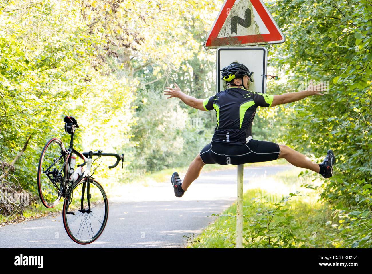 Un cycliste qui tombe heurte un panneau de signalisation indiquant qu'il y a une route dans les virages. Banque D'Images
