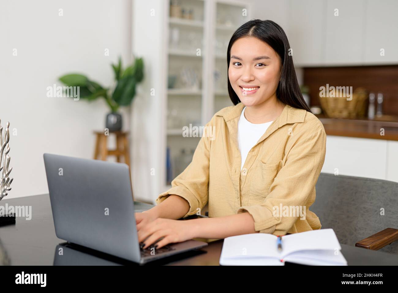 Femme asiatique intelligente regardant l'appareil photo, assise à la réception devant un ordinateur portable.Femme d'affaires prospère appréciant son travail, prête pour le prochain défi Banque D'Images