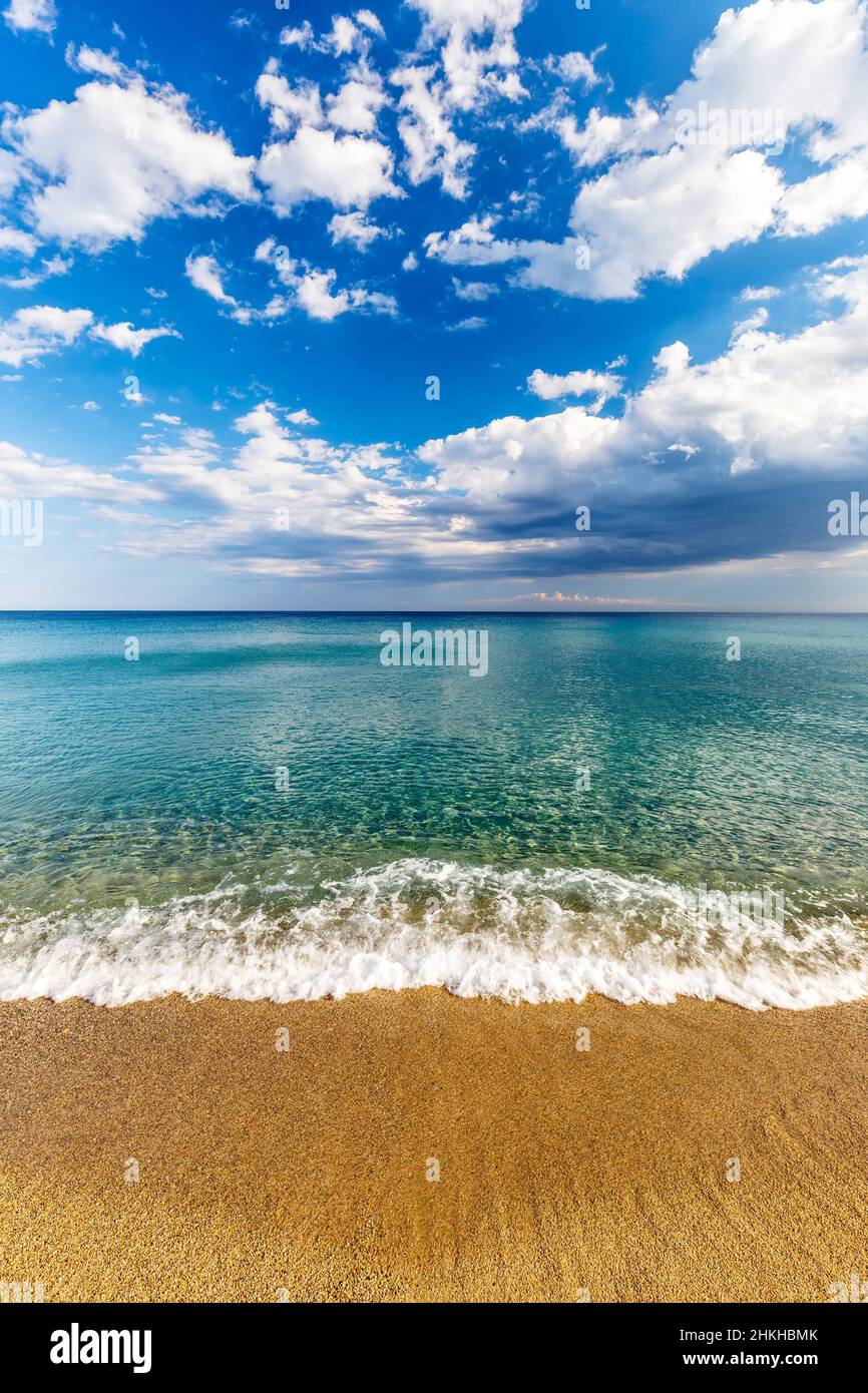 Mer turquoise calme et nuages sur ciel bleu en Italie, Europe.Petites vagues sur une plage de sable au premier plan. Banque D'Images