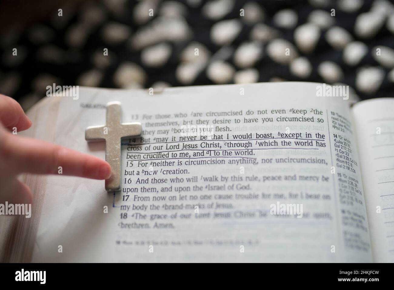 Main de l'enfant pointant vers la croix sur la page de la Bible avec le verset souligné Banque D'Images
