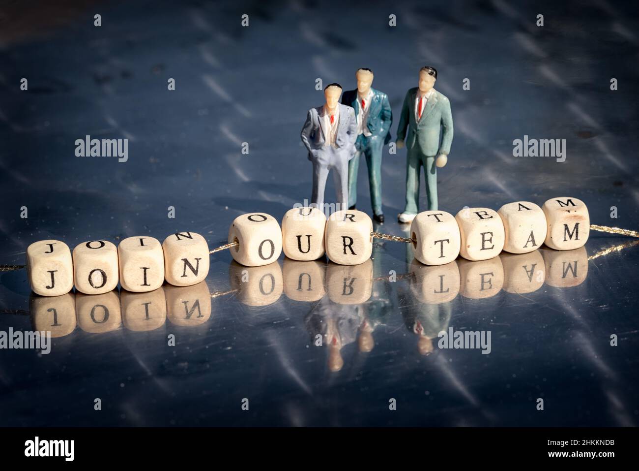 Modèle miniature d'hommes d'affaires et cubes en bois avec inscription de notre équipe sur un fil sur une table réfléchissante.L'entreprise de recrutement concep Banque D'Images