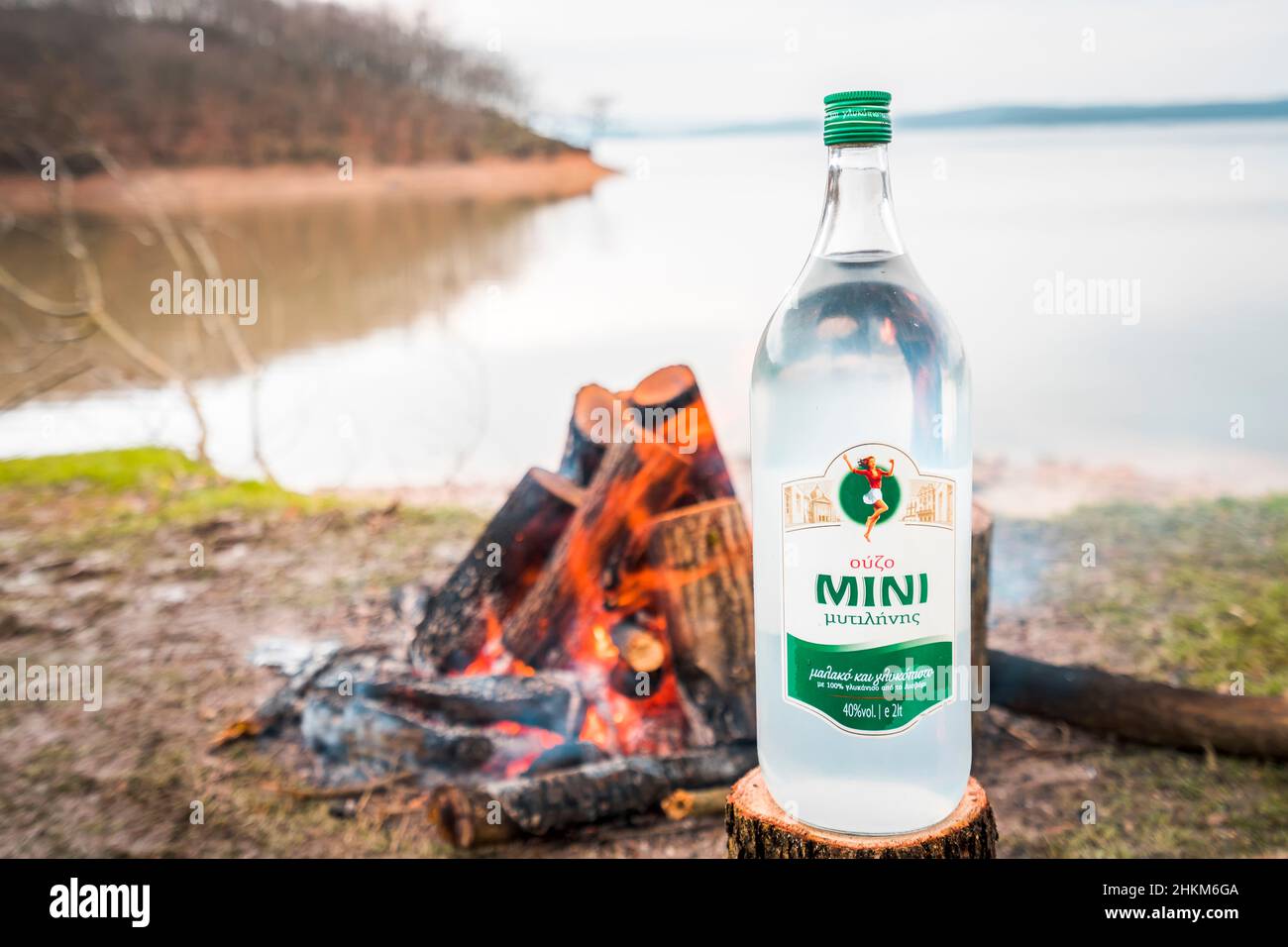 Bouteille de boisson alcoolisée à l'anis grec Ouzo sur une souche d'arbre avec feu de camp en arrière-plan. Banque D'Images