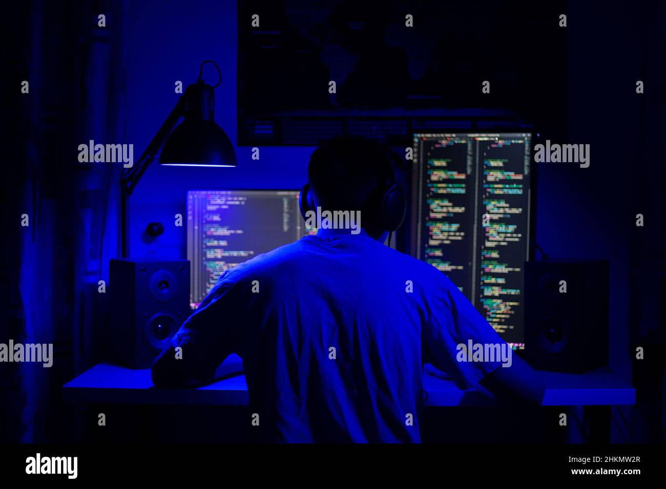 Un homme s'assoit à un ordinateur dans une pièce à une table la nuit avec un éclairage bleu et des programmes Banque D'Images