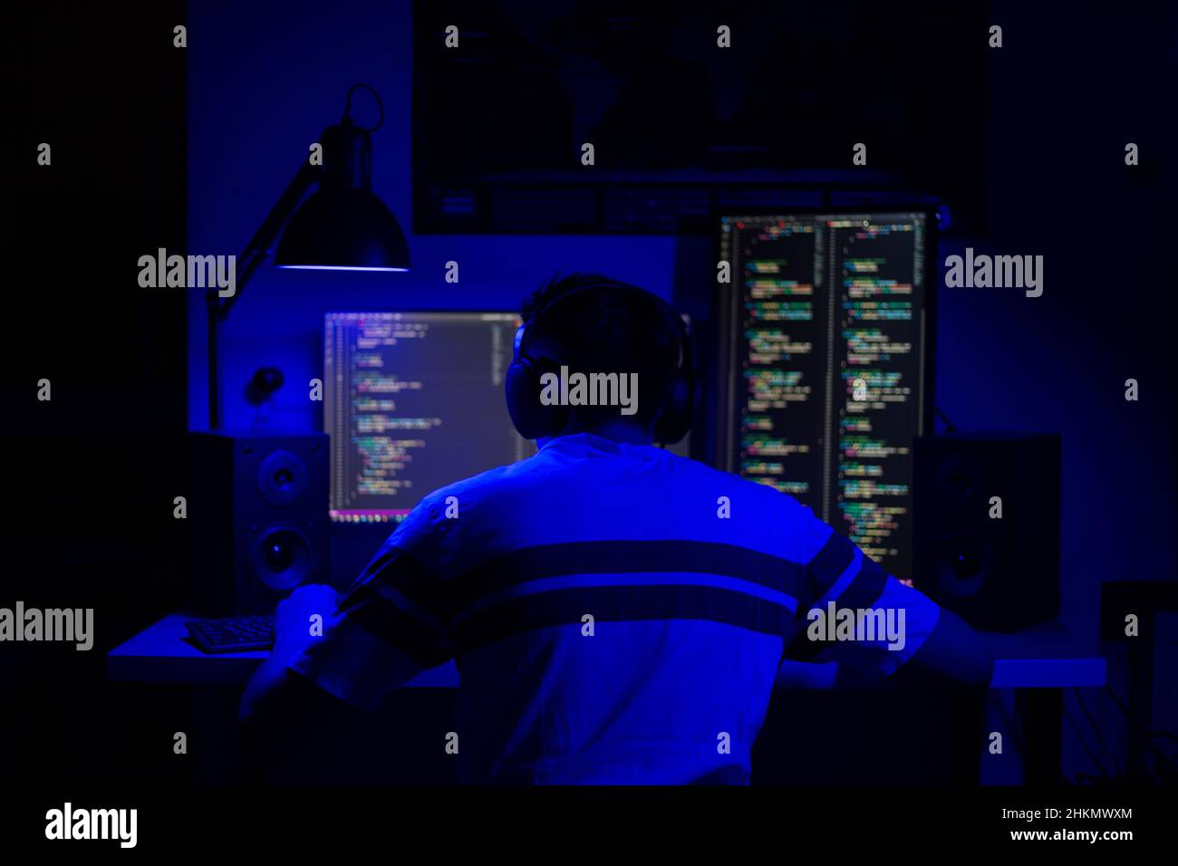 Un homme s'assoit à un ordinateur dans une pièce à une table la nuit avec un éclairage bleu et des programmes Banque D'Images