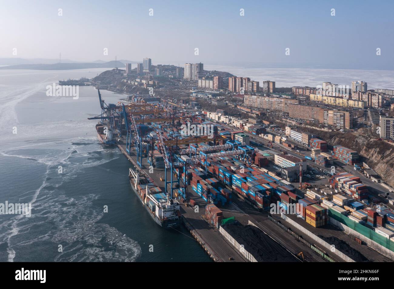 Vladivostok, Russie - 27 janvier 2022 : Vue de dessus du terminal des conteneurs du port maritime et de la ville.En hiver, un bateau à conteneurs est en train de charger au quai. Banque D'Images