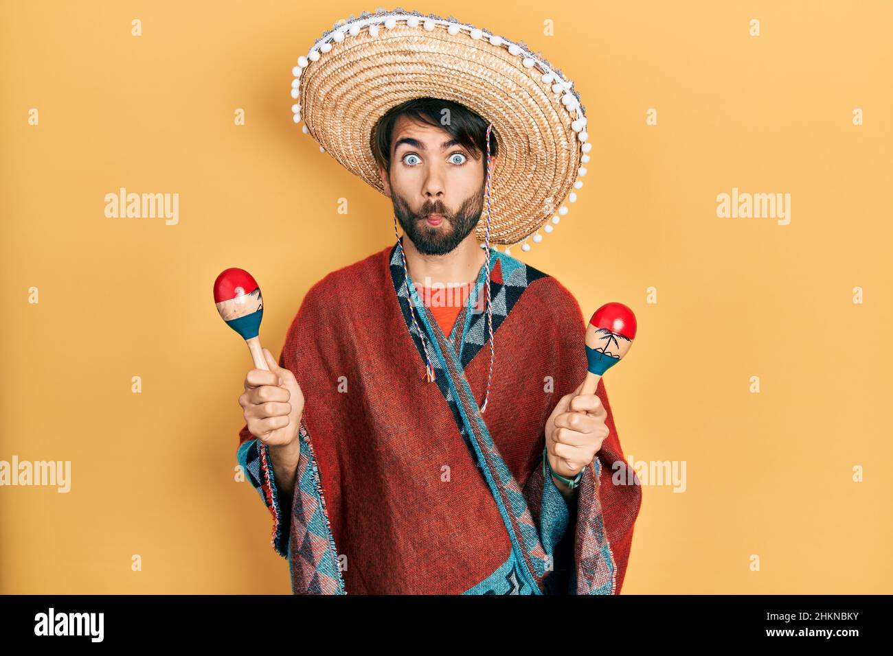 Jeune homme hispanique portant un chapeau mexicain tenant des maracas  faisant le visage de poisson avec la bouche et les yeux de bourdonner, fou  et comique Photo Stock - Alamy