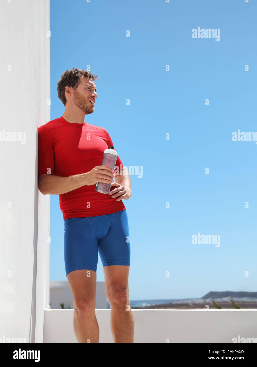 Athlète homme coureur buvant sports bouteille d'eau entraînement à la maison balcon ou à l'extérieur de la salle de gym épuisé avoir coup de chaleur.Récolte verticale du corps musculaire Banque D'Images