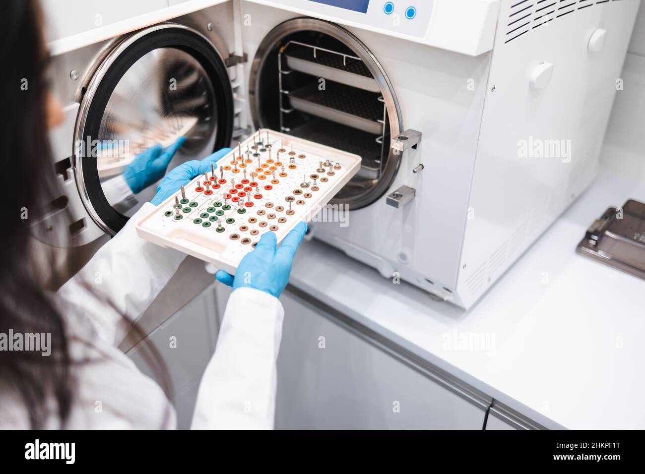 Gros plan d'une assistante dentaire féminine qui met un instrument dentaire dans un autoclave.Stérilisation de l'ensemble pour implantation chirurgicale dentaire Banque D'Images