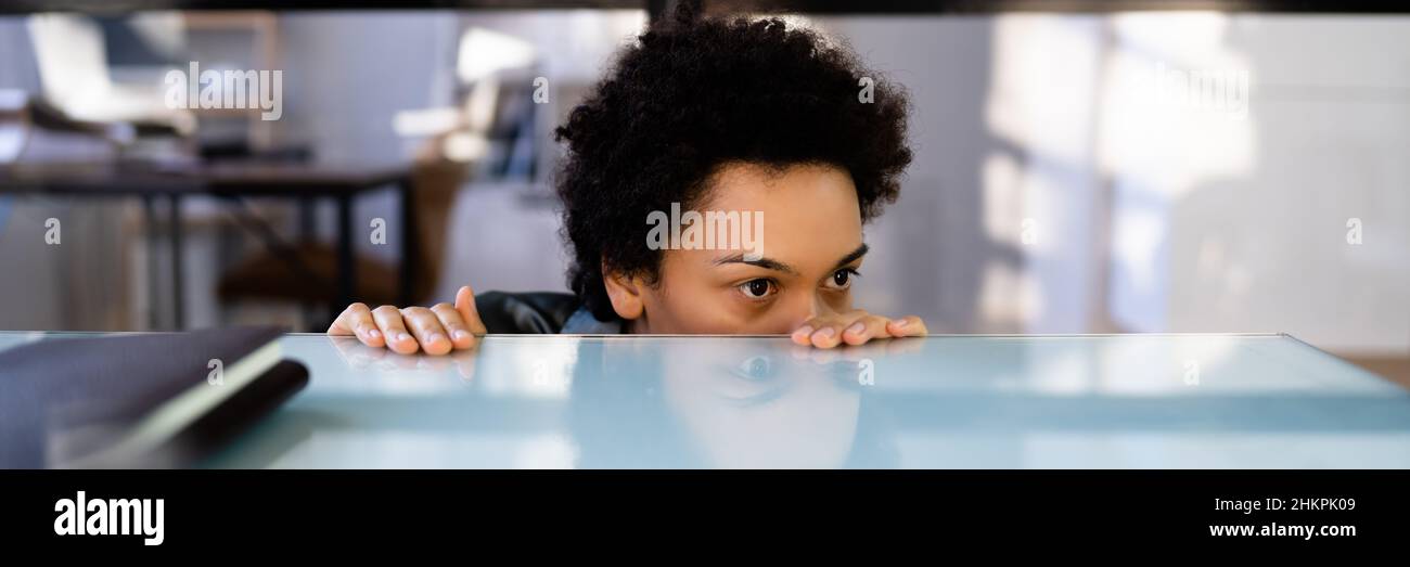 Femme effrayée se faisant cacher sous le bureau dans le bureau Banque D'Images