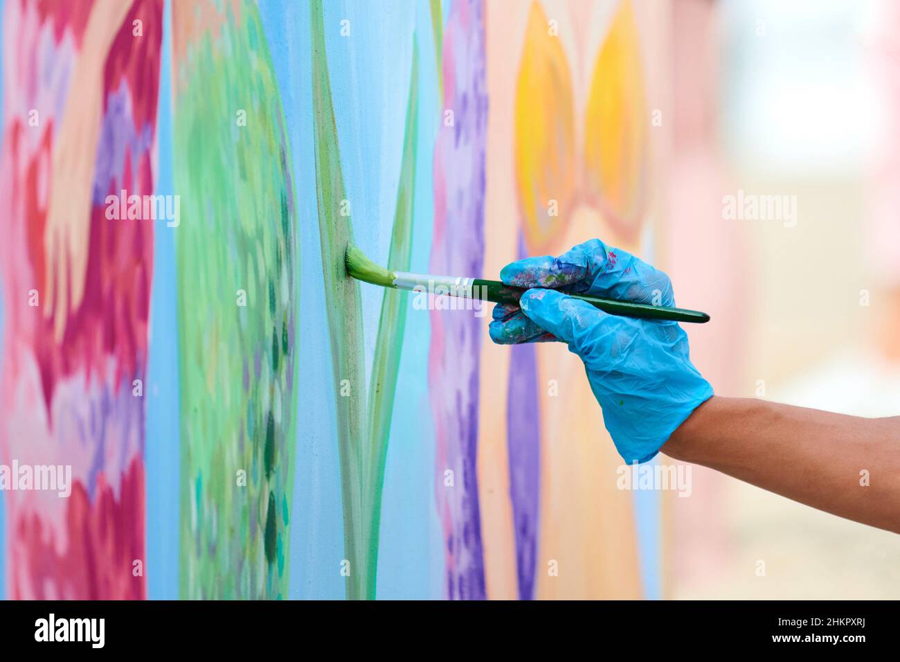 La main de l'artiste avec un pinceau peint en couleurs sur toile lors d'un festival d'art en plein air.Femme peintre en gants bleus dessine une image surréaliste avec pai Banque D'Images