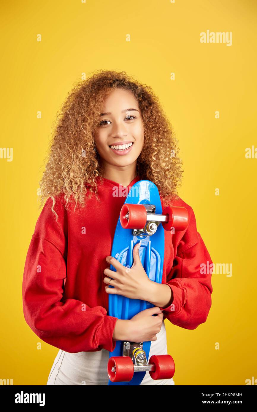 Ravie de jeunes Afro-américaines hipster dans le sweat à capuche et avec panneau de penny regardant la caméra sur fond jaune Banque D'Images