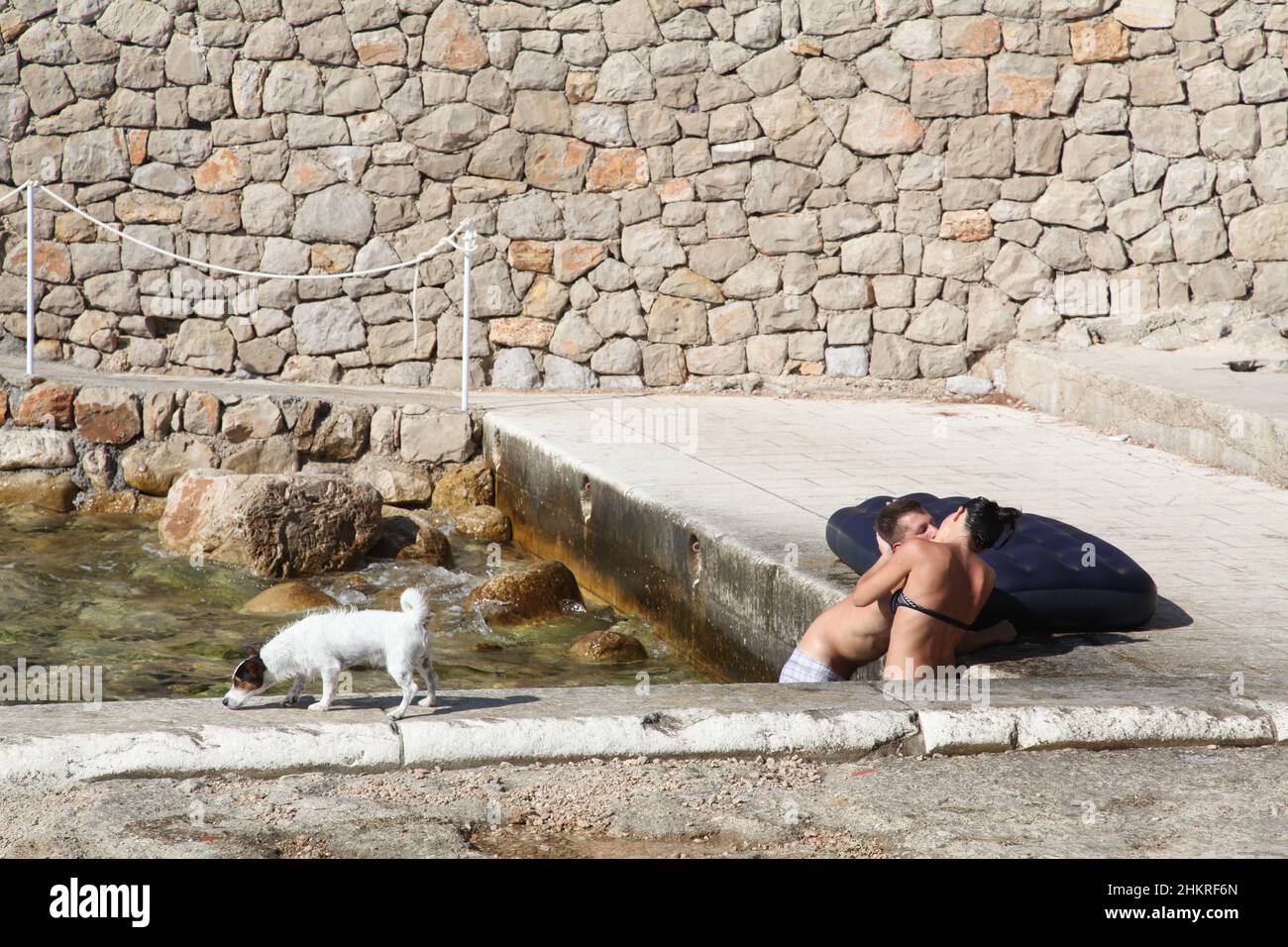 Un jeune couple aime l'après-midi d'été s'embrasser dans l'eau sur la plage de Dubrovnik, tandis que son petit chien aime son temps étudiant où se trouver Banque D'Images