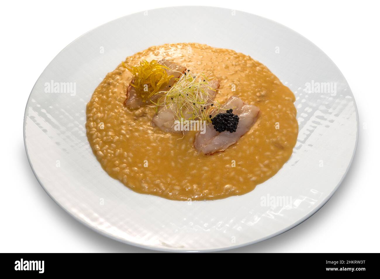 Risotto aux langoustines crues avec pousses, zeste de citron caramélisé et caviar.Dans un plat blanc isolé sur blanc Banque D'Images