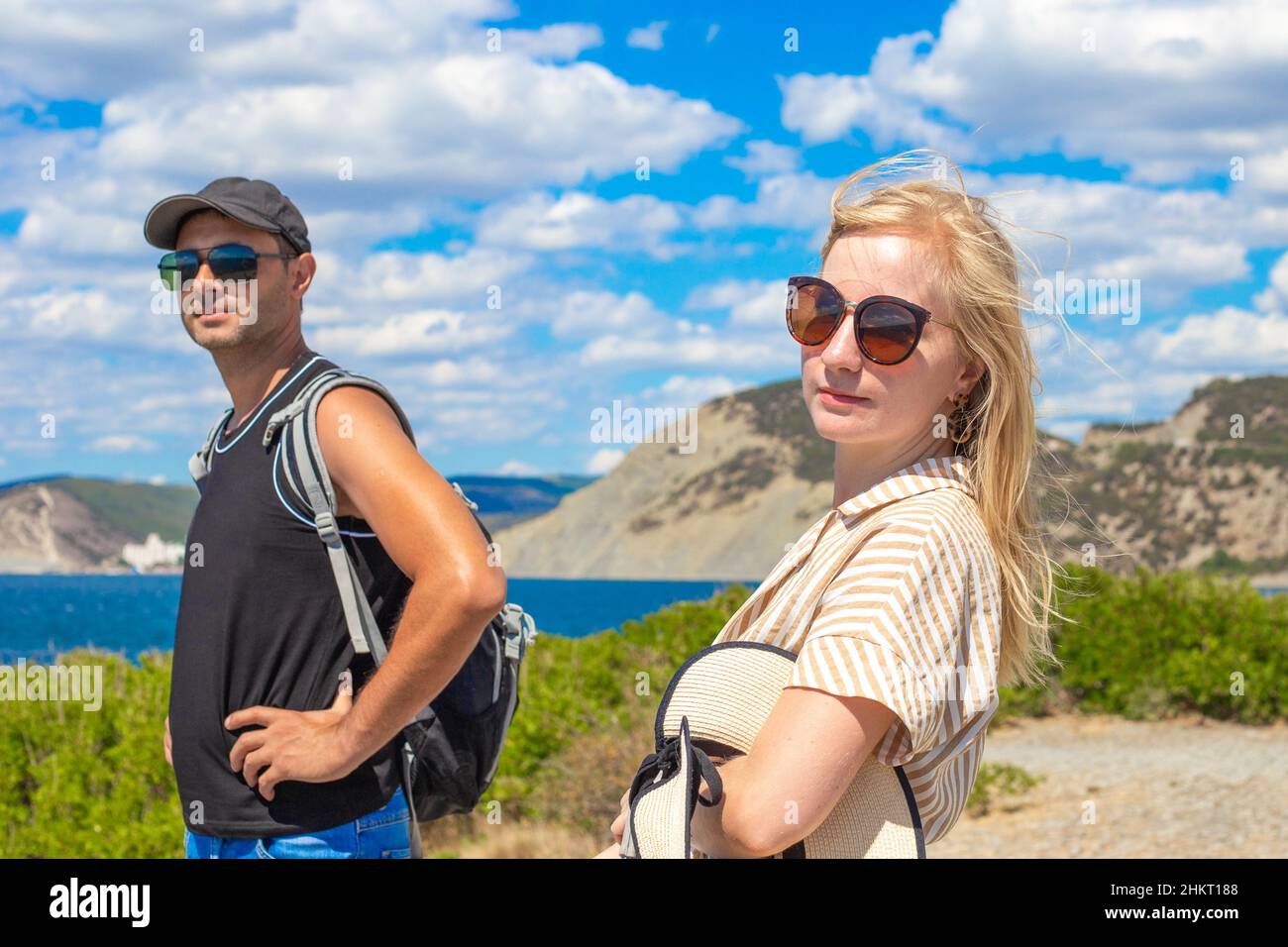 Une femme blonde et un homme en casquette marchent sur fond de mer et de collines.Voyages et randonnées. Banque D'Images