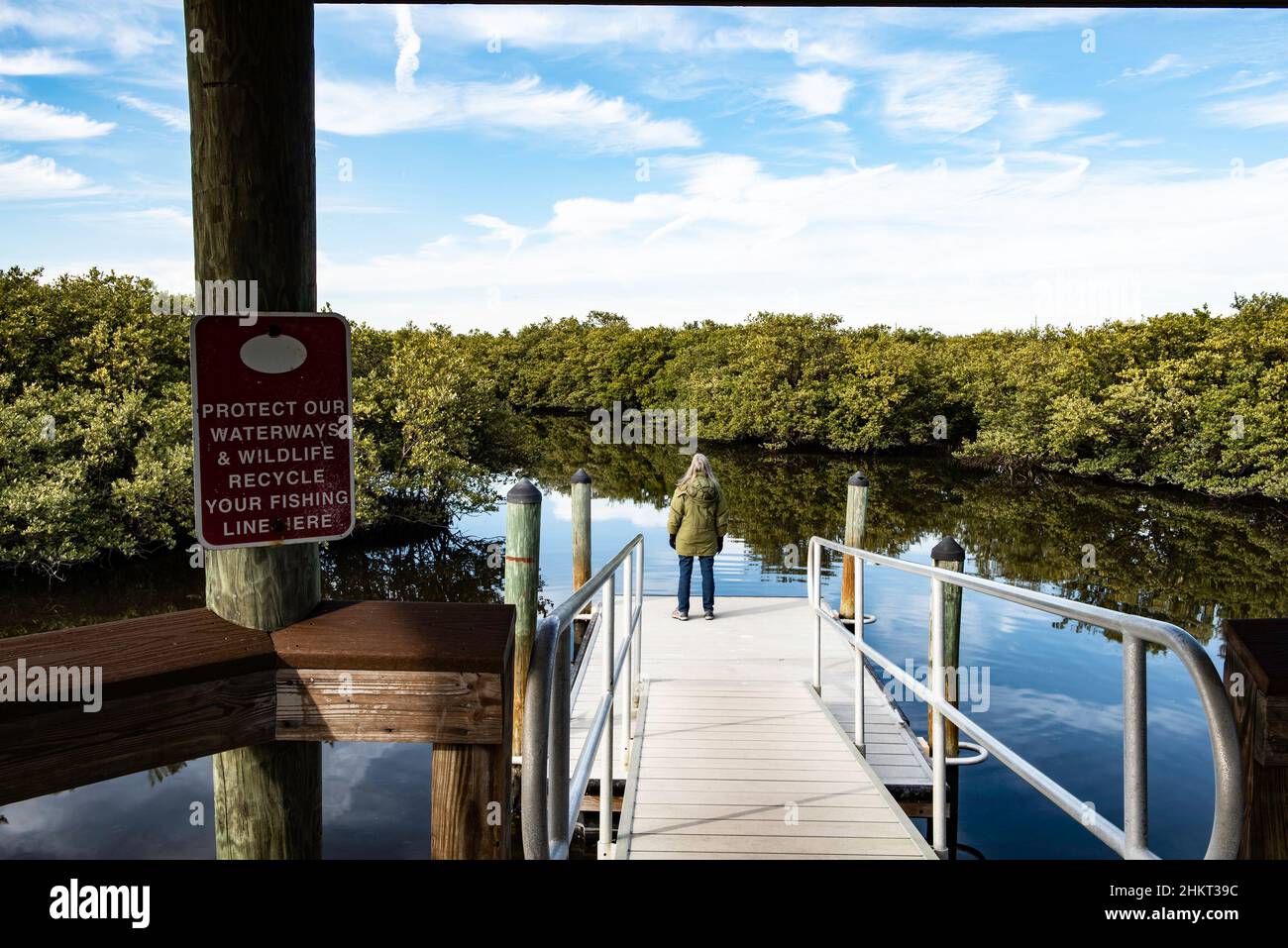 Une vue arrière d'une femme mature de 50-60 ans avec de longs cheveux gris et portant une parka debout sur un quai flottant dans la réserve de Ponce Inlet, en Floride Banque D'Images