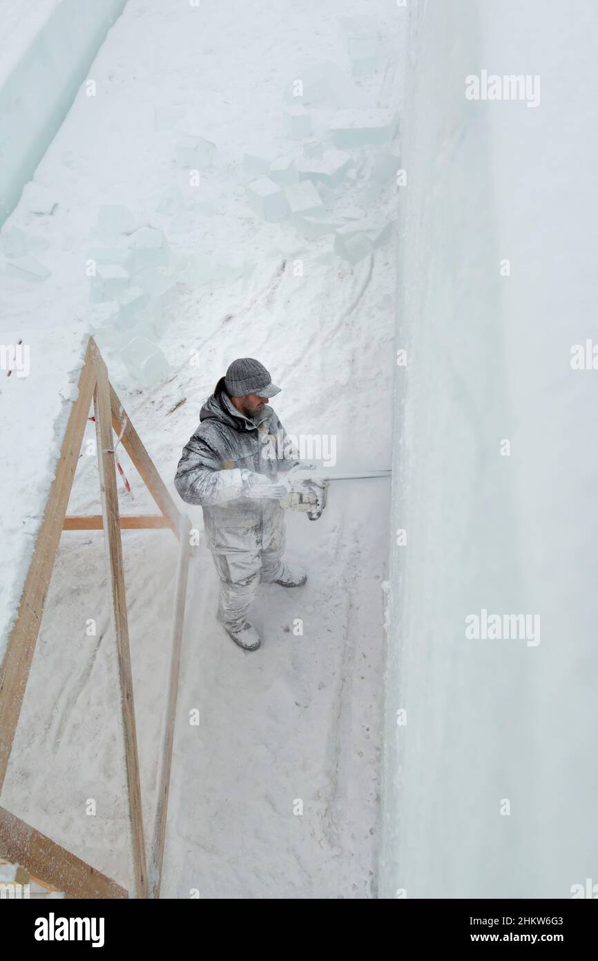 Le sculpteur élimine les contours de la composition future avec une tronçonneuse dans une dalle de glace Banque D'Images