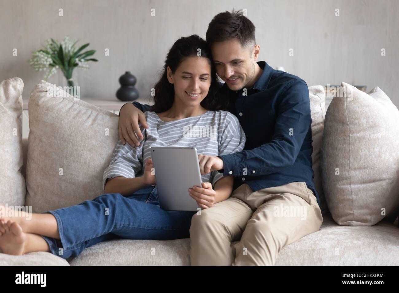 Jeune couple souriant utilisant une tablette ensemble, assis sur un canapé Banque D'Images