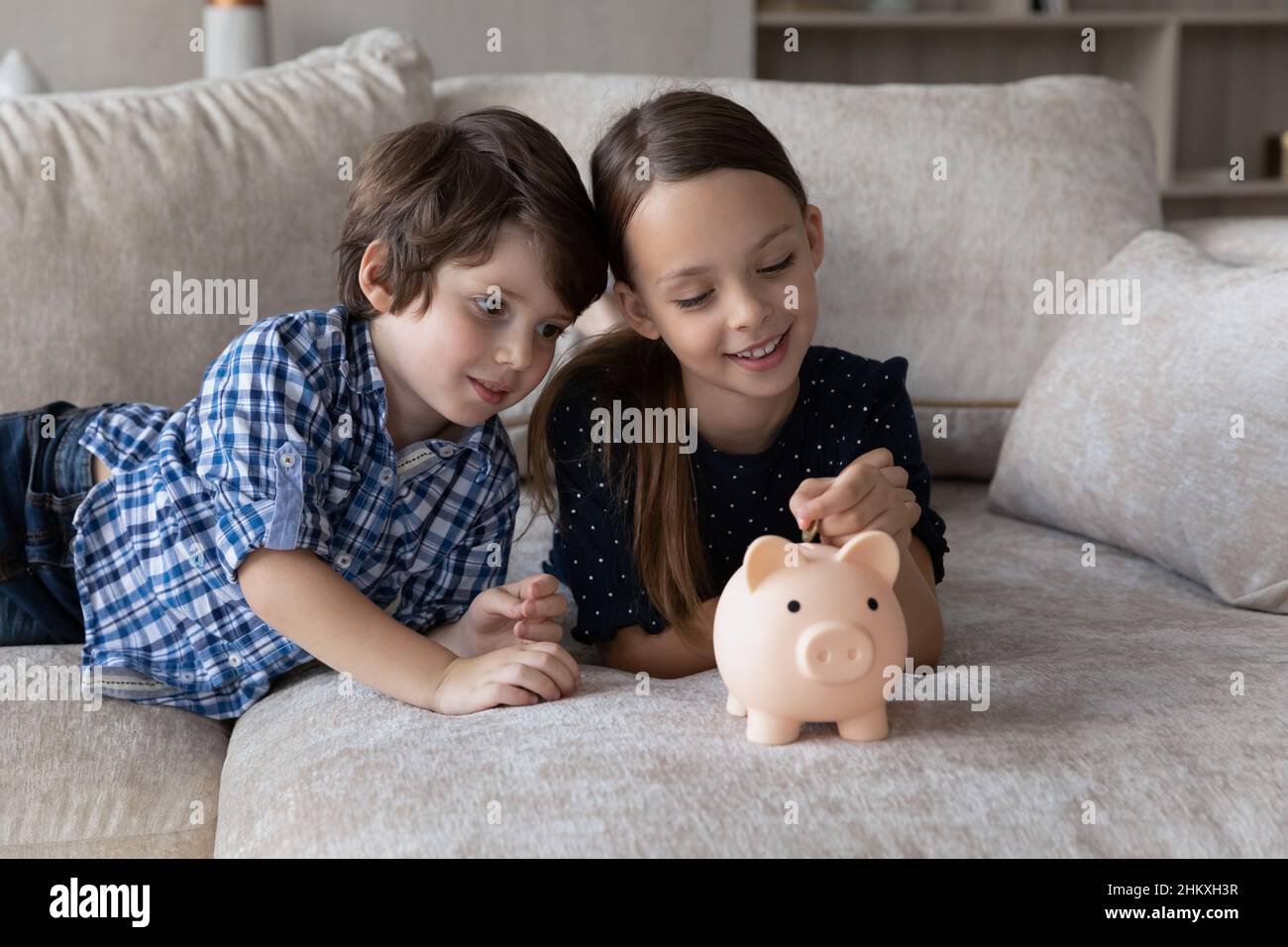 Un garçon souriant et une fille mettant la pièce de monnaie dans une banque de porc rose Banque D'Images