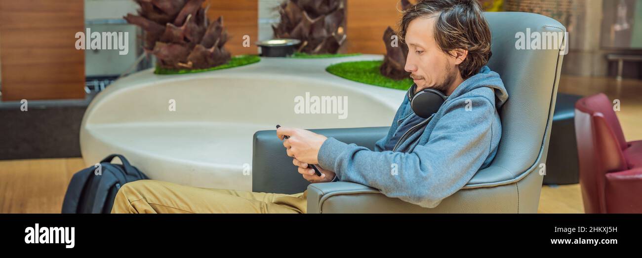 Un homme dans le salon à l'aéroport est en attente de son avion, utilise un smartphone et un casque. Young smiling man with beard en holding smartphone Banque D'Images