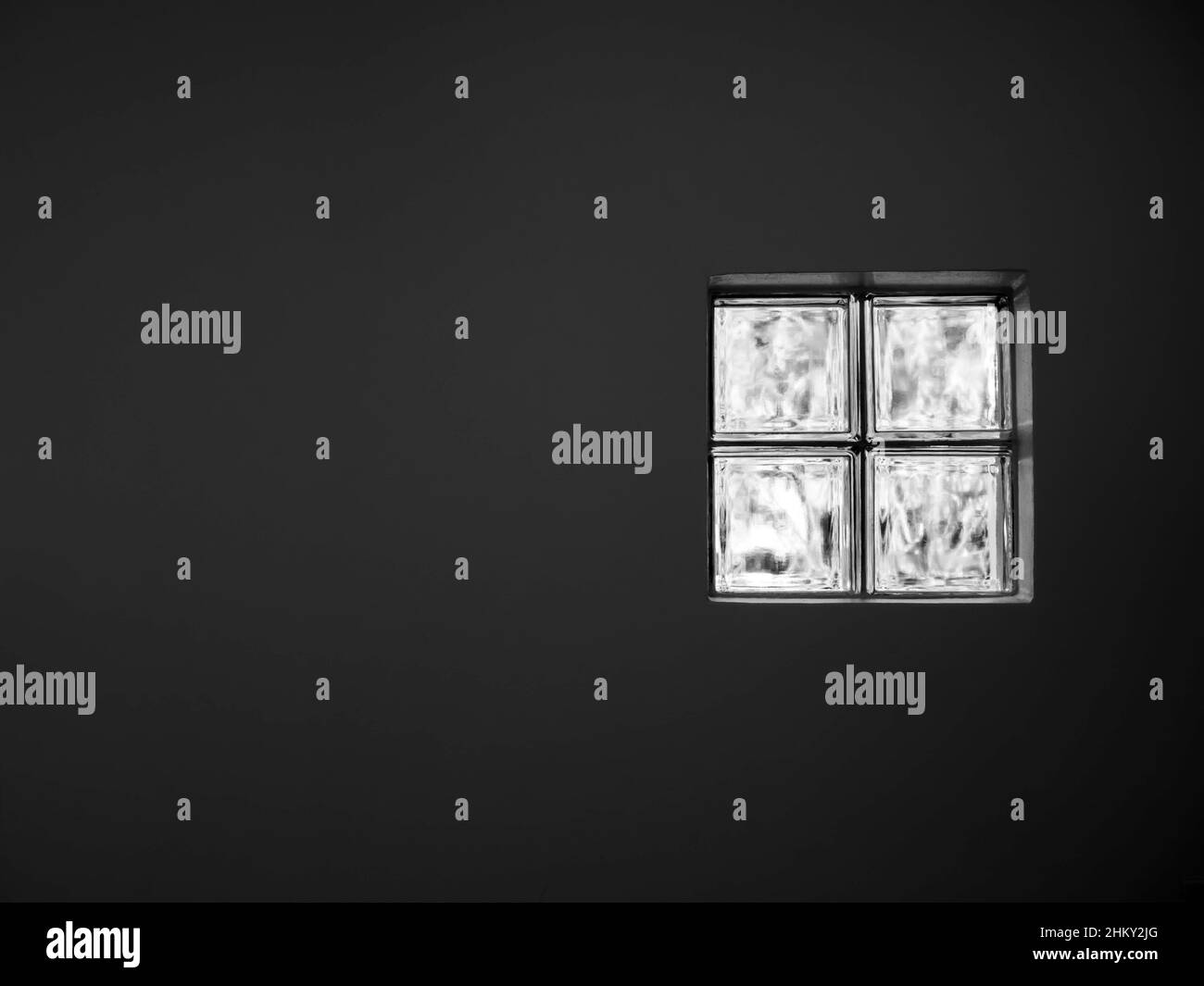 Gros plan de quatre blocs de verre, briques de fenêtre, un canal éclairé pour la lumière à travers sur le fond blanc de mur avec espace de copie, pièce sombre. Banque D'Images