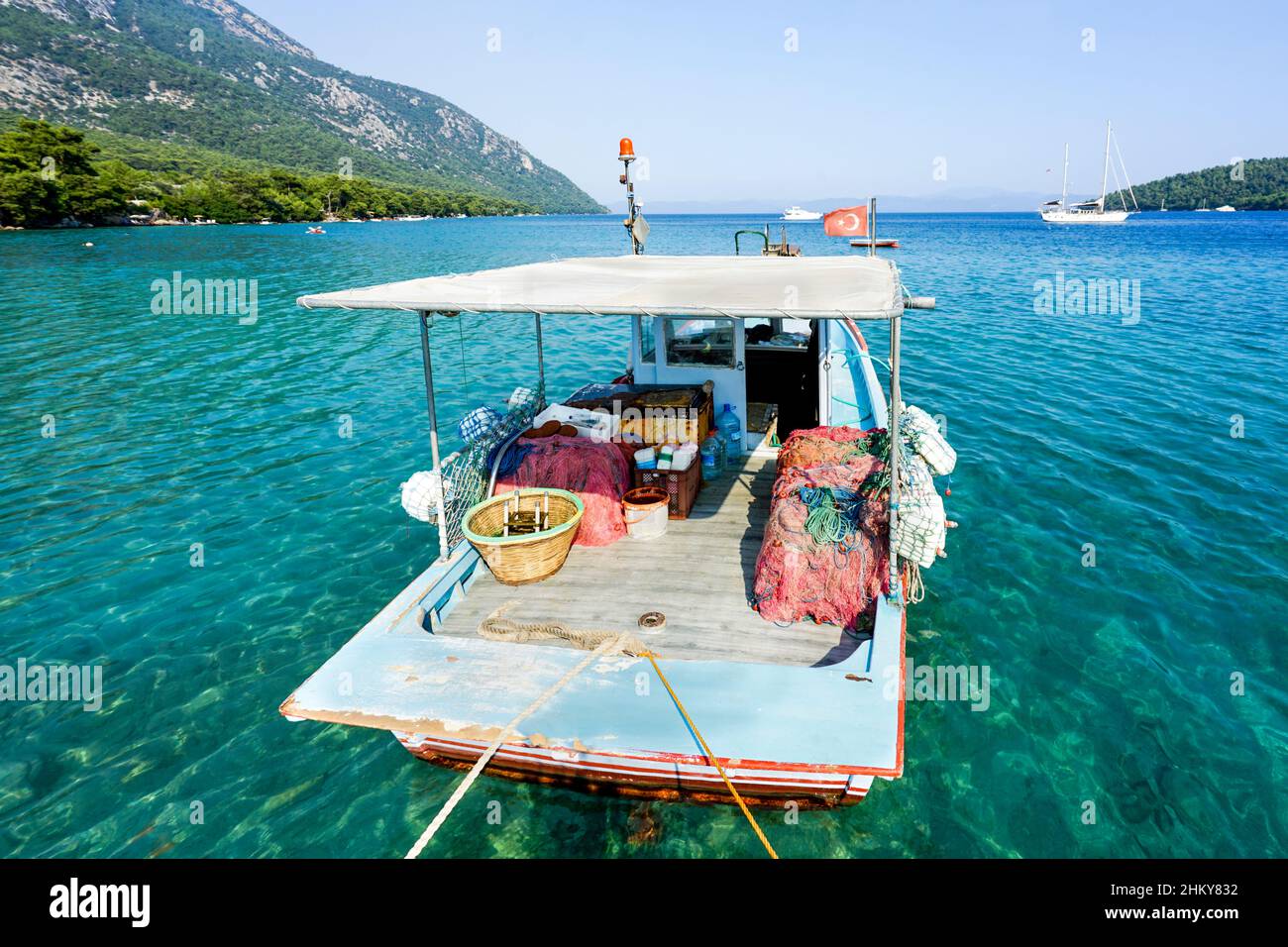 Un petit bateau de pêche bleu dans la mer attaché avec corde dans le port.Vue dégagée sur la plage d'Akbuk Cove (baie) dans la province de Mugla, dans le sud-ouest de la Turquie. Banque D'Images