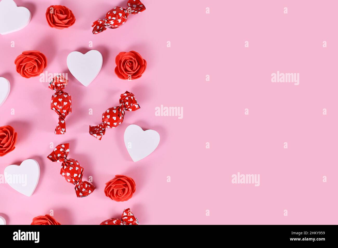 Bonbons de Saint-Valentin, confettis en forme de coeur et roses rouges sur le côté de fond rose avec espace de copie Banque D'Images