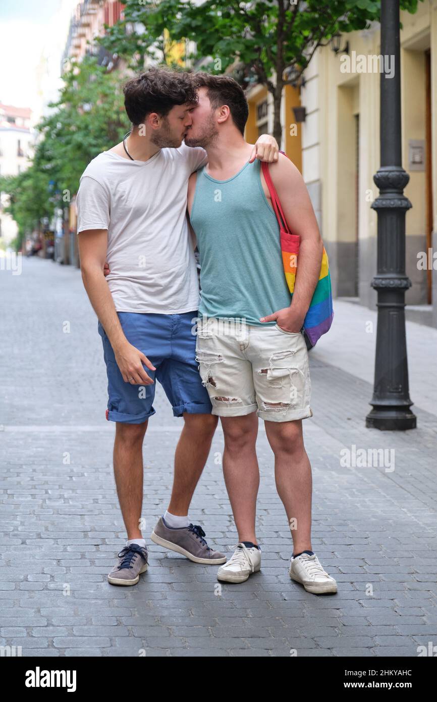 Un couple gay riant et embrassant assis sur un banc tenant des drapeaux LGBT. Banque D'Images