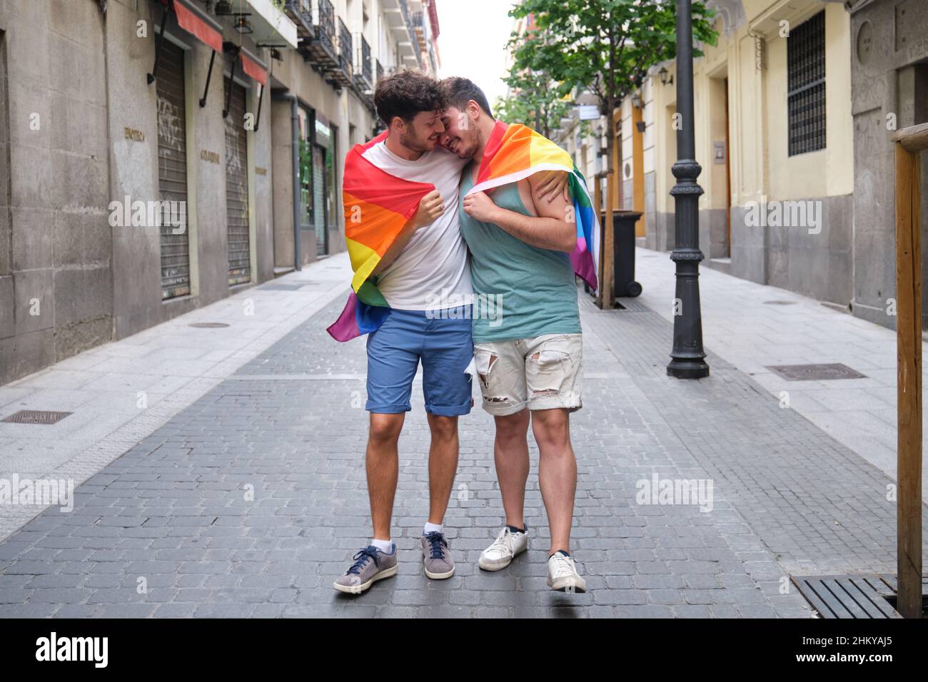 Couple gay enveloppé dans un drapeau LGBT, embrassant et souriant. Banque D'Images
