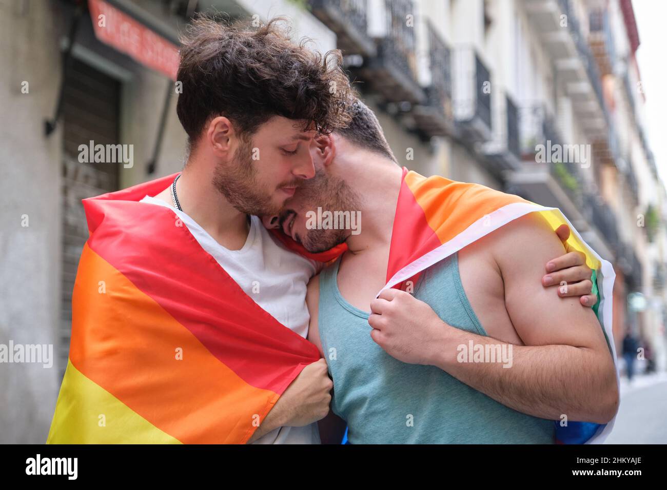 Couple gay enveloppé dans un drapeau LGBT, embrassant et souriant. Banque D'Images