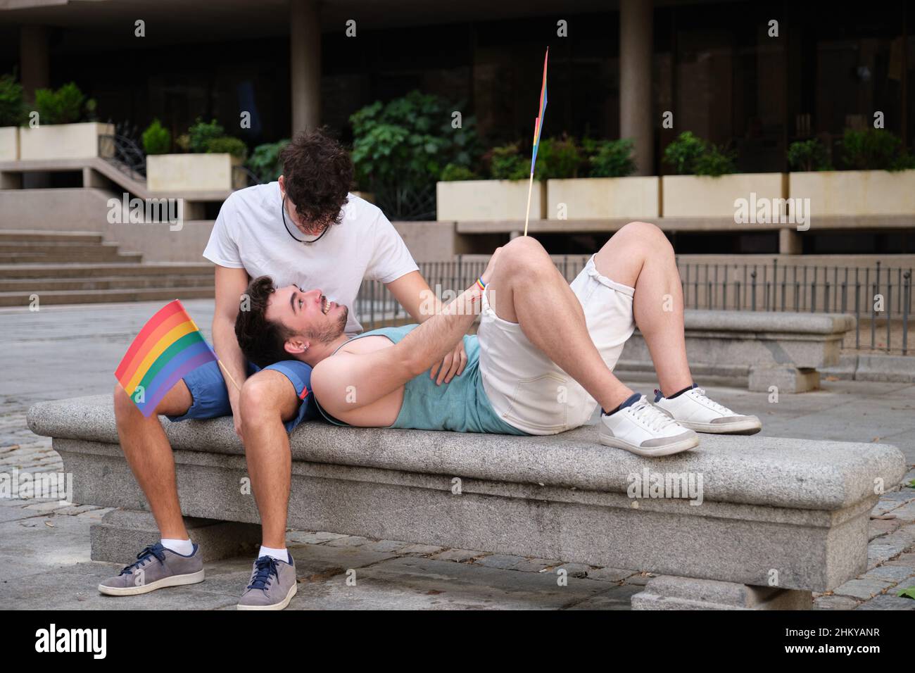 Un couple gay riant et embrassant assis sur un banc tenant des drapeaux LGBT. Banque D'Images