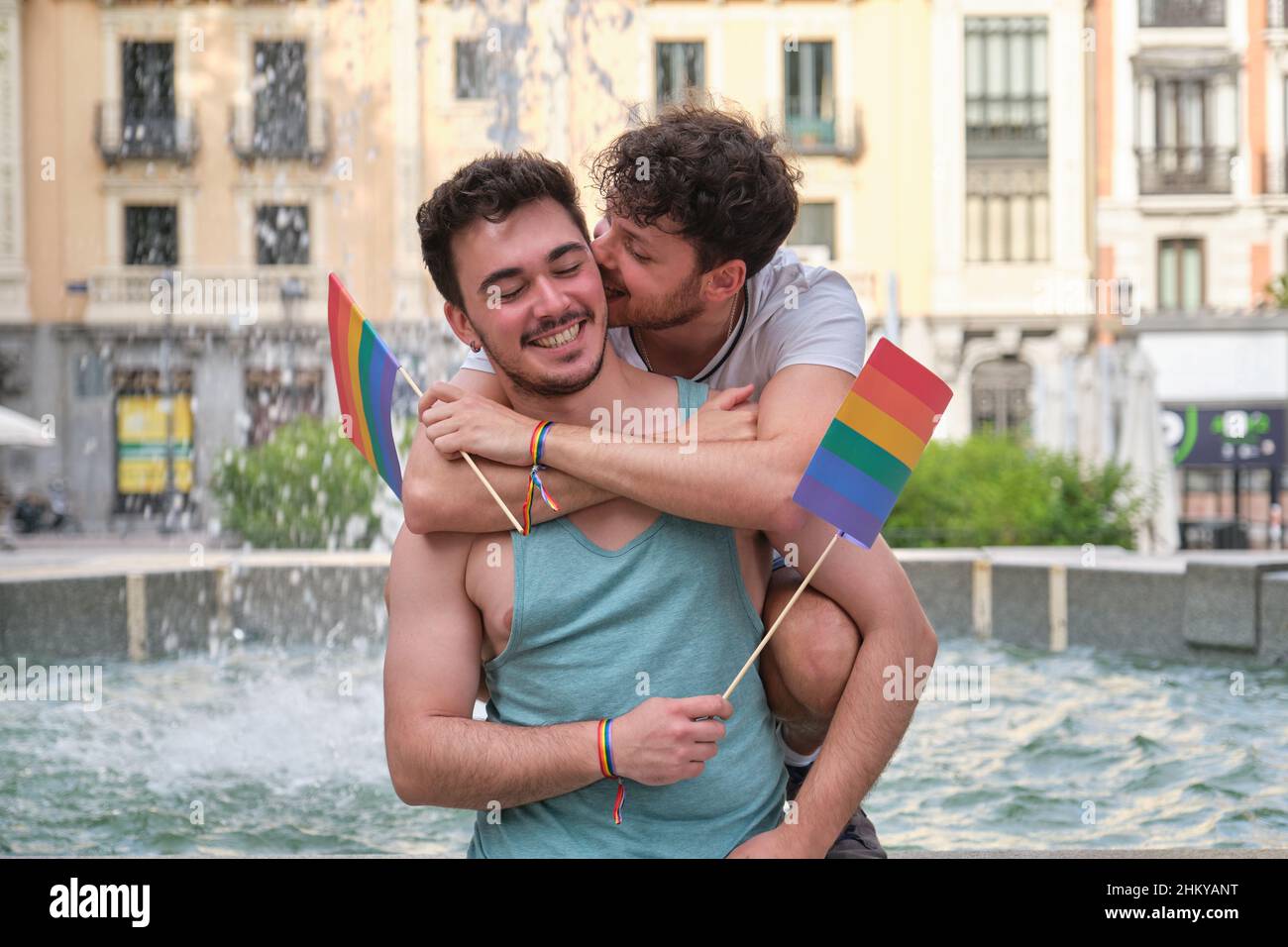 Un homme gay piquant l'oreille de son ami tout en embrassant et en riant en tenant des drapeaux LGBT. Banque D'Images