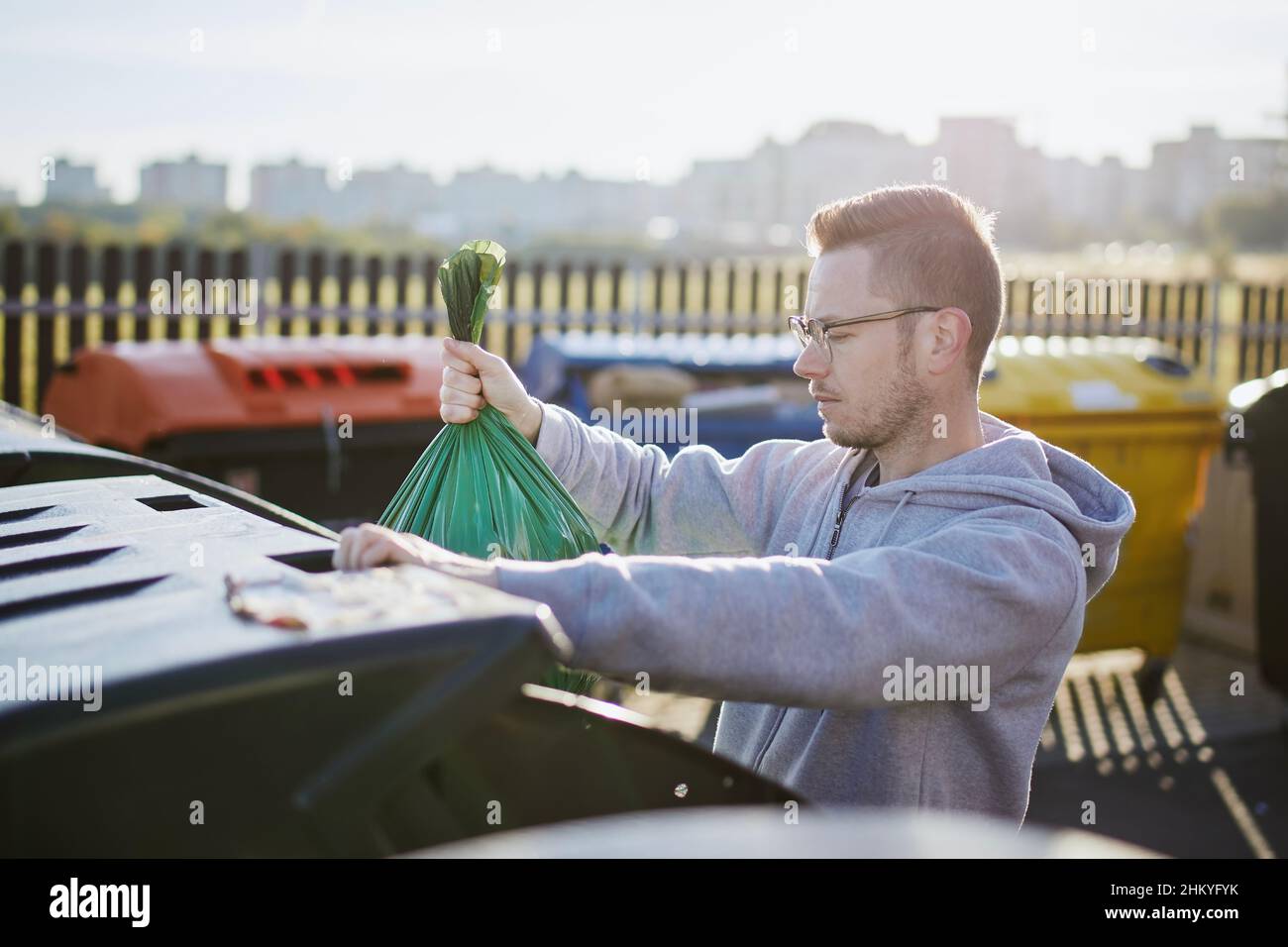 Homme marchant avec des ordures.Personne jetant le sac en plastique vert à la poubelle sur la rue de la ville. Banque D'Images