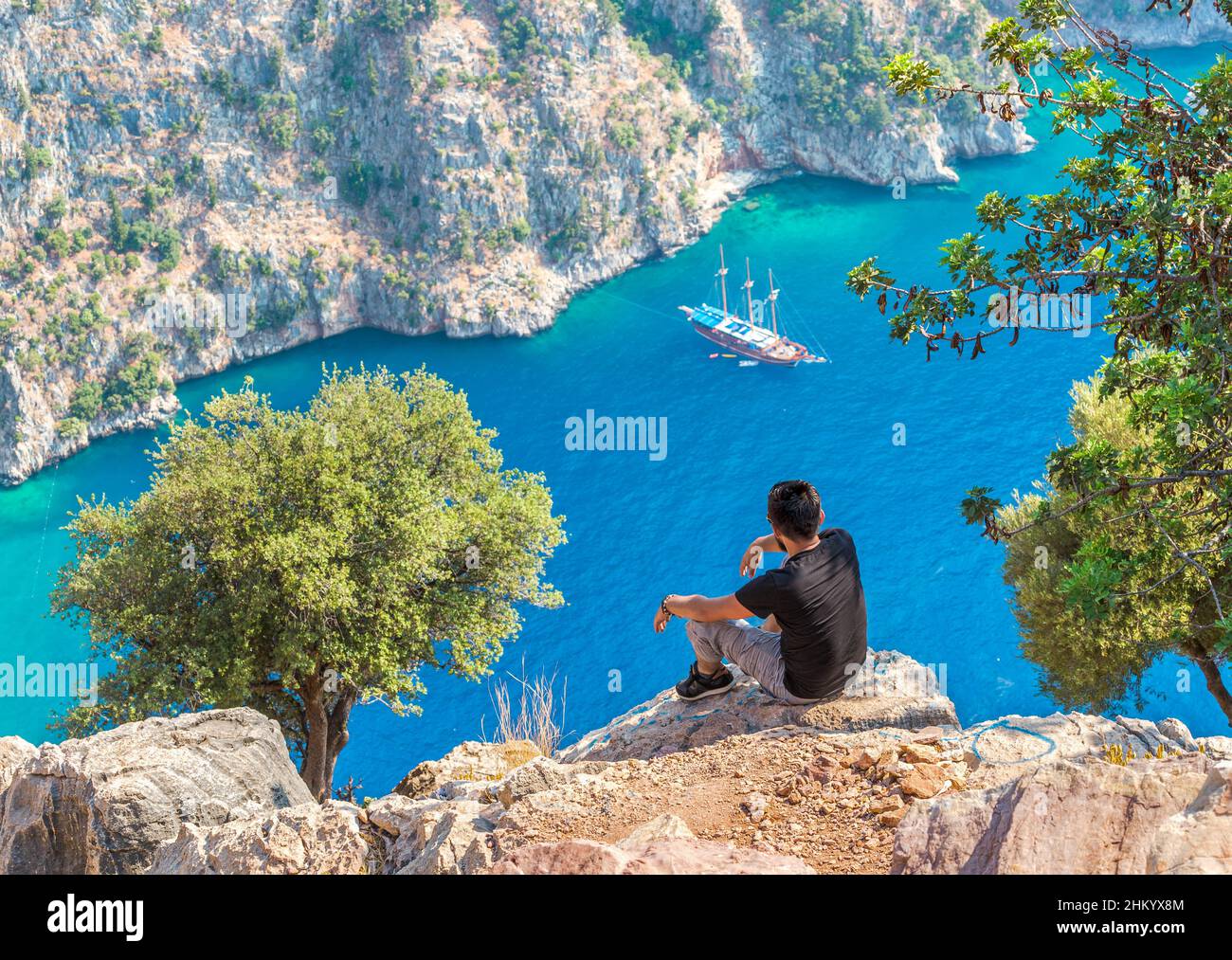 Turc assis au bord d'une falaise et appréciant le magnifique paysage de la mer.Vue sur Butterfly Valley en Turquie. Banque D'Images