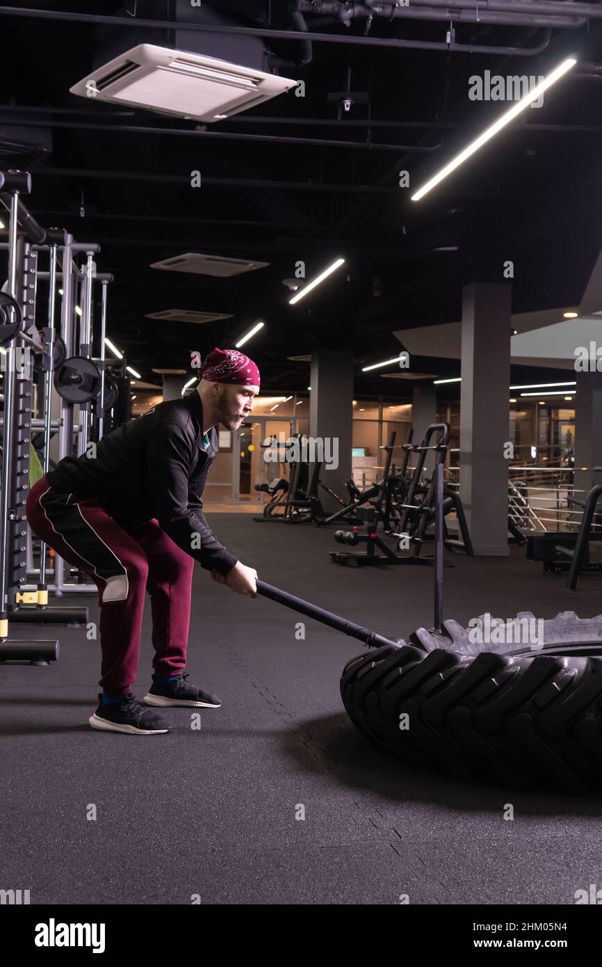 Un homme frappe une roue de sledgehammer en forme physique, le concept d'un style de vie sain homme sledgehammer marteau actif, de la salle de gym musclé pour l'athlète Banque D'Images