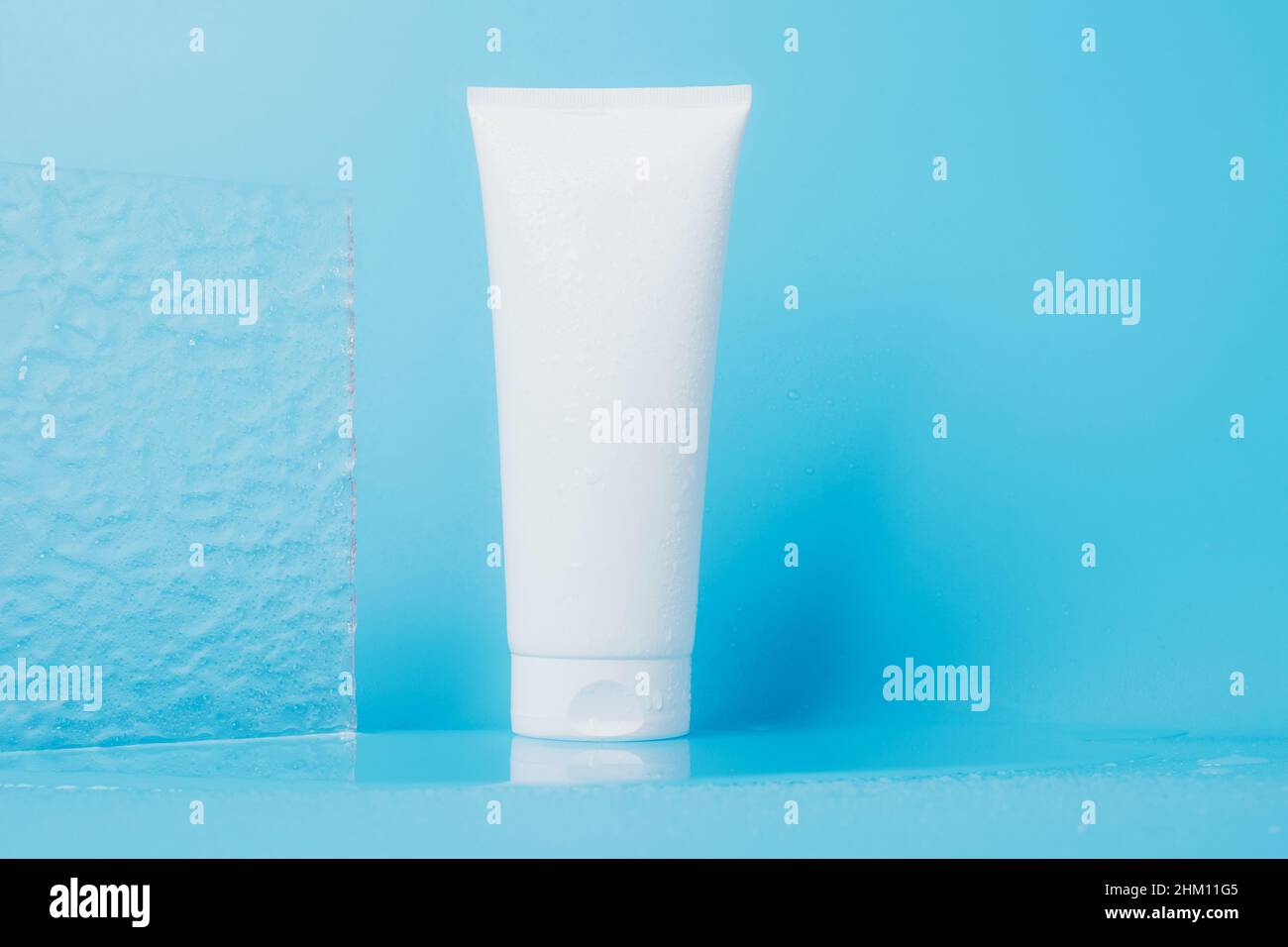 Produit cosmétique en tube éclaboussures et gouttes d'eau sur fond bleu.Shampooing, gel, emballage blanc baume Banque D'Images