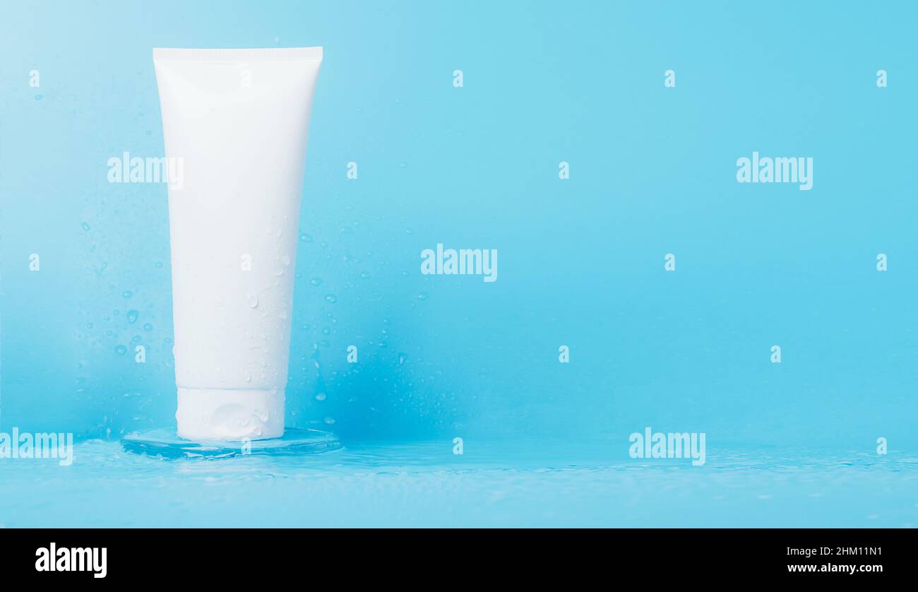 Produit cosmétique en tube éclaboussures et gouttes d'eau sur fond bleu.Shampooing, gel, emballage blanc baume Banque D'Images