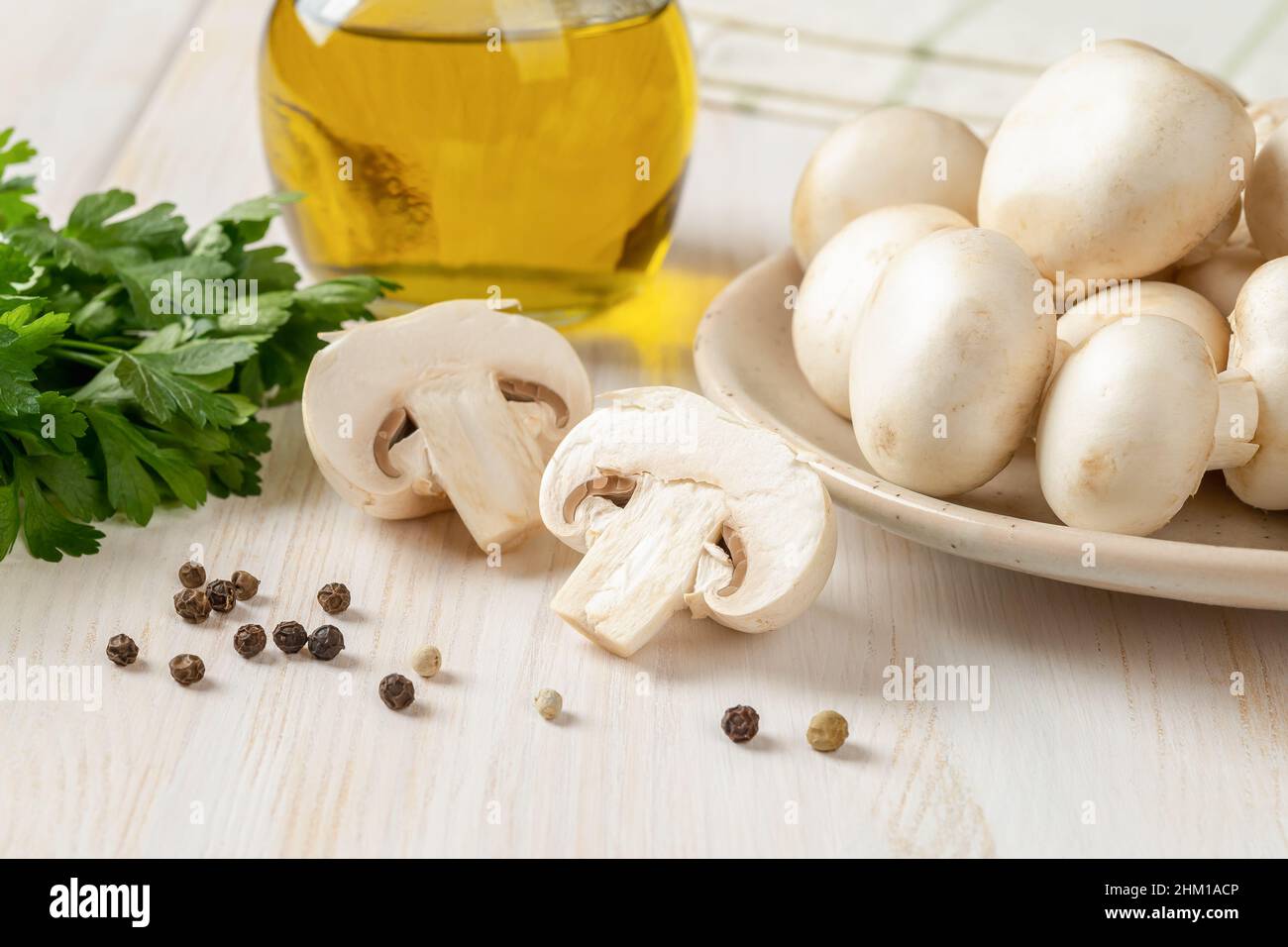 Gros plan de champignon cru coupé en deux, champignons de Paris entiers, persil vert et pot d'huile d'olive sur une table en bois blanc.Cuisson de champignons blancs frais Banque D'Images