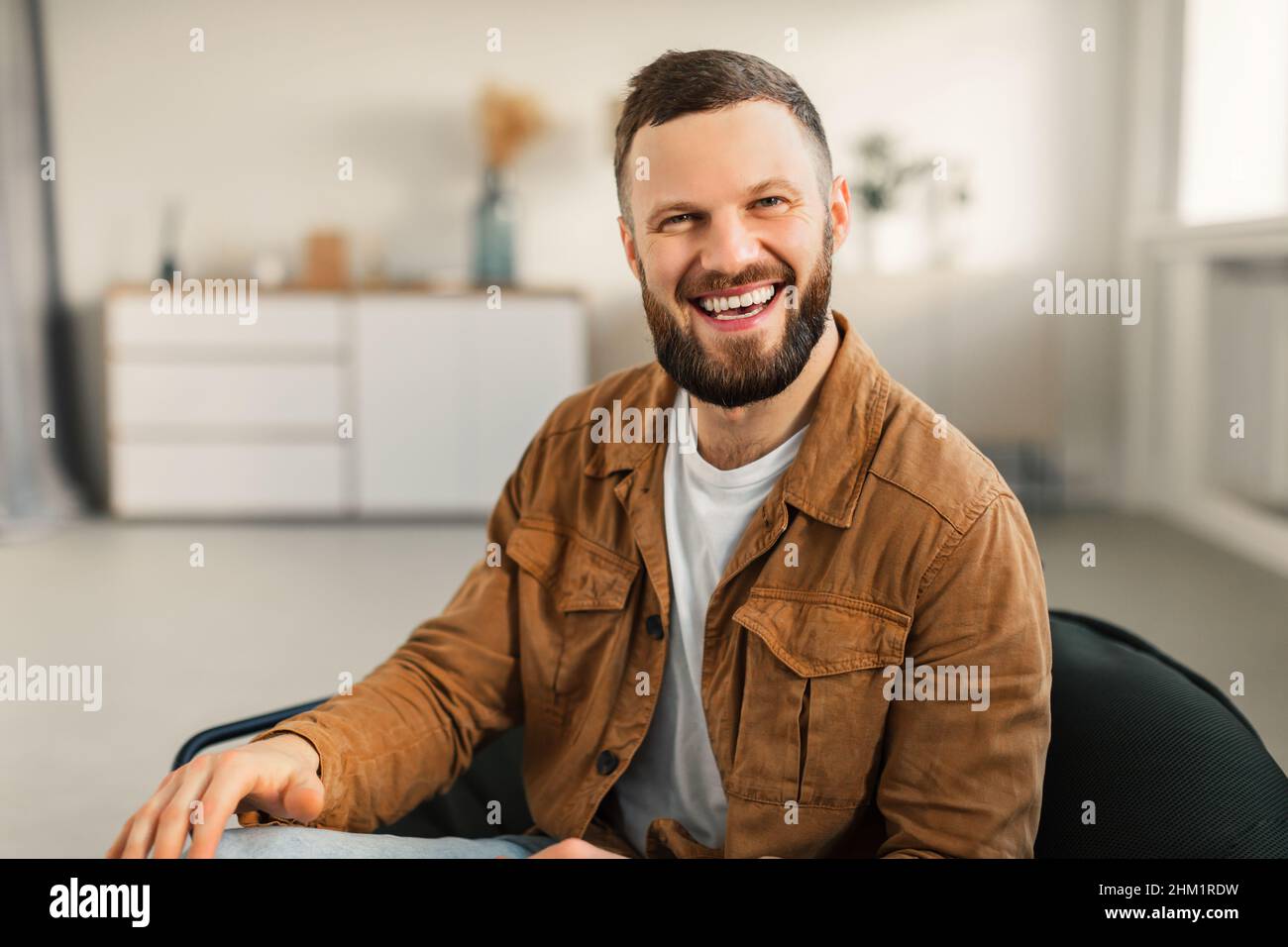 Joyeux barbu Guy souriant assis dans la chaise à la maison Banque D'Images