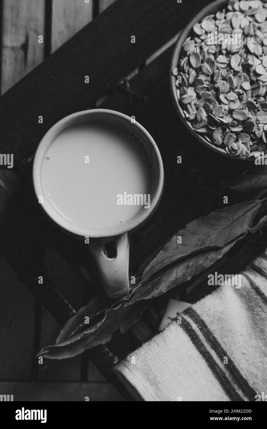 Un petit déjeuner d'une tasse de lait d'avoine avec des graines d'avoine sur une planche en bois en noir et blanc Banque D'Images