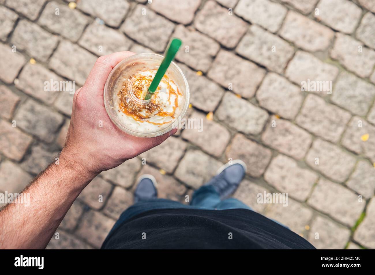 Homme debout sur un sol en brique et boit du café au caramel dans une tasse en plastique. Style de vie personne pov point de vue tourné Banque D'Images
