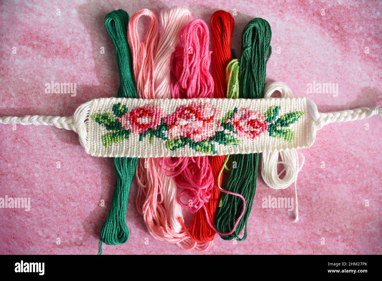 Bracelet d'amitié tissé avec motif de fleur brillant Rose près des skeins de fil de broderie Banque D'Images