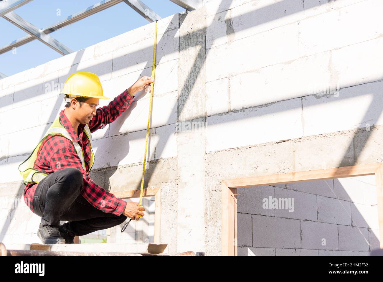 Travailleur de la construction ou entrepreneur qui utilise du ruban de mesure pour vérifier le cadre de toit en acier jusqu'à la porte sur le chantier de construction, le contremaître prenant m Banque D'Images